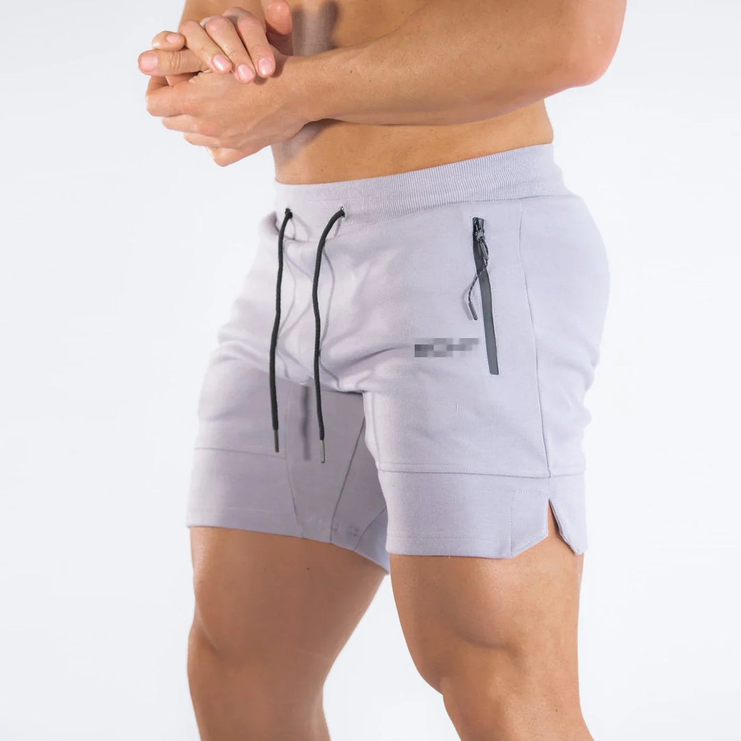 Male model wearing light gray athletic shorts with black drawstrings and zippered pocket detail