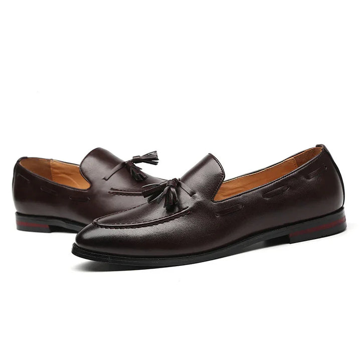 Dark brown leather men's tassel loafers with black soles and red accent heel detail