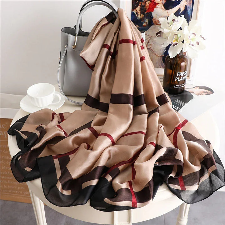 Beige and black striped silk scarf draped over white round table with gray handbag, white teacup, and vase with white flowers