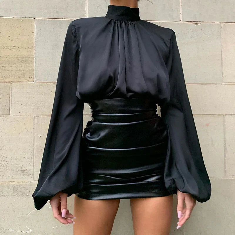 Woman wearing black high-neck long sleeve blouse with puff sleeves and black satin mini skirt