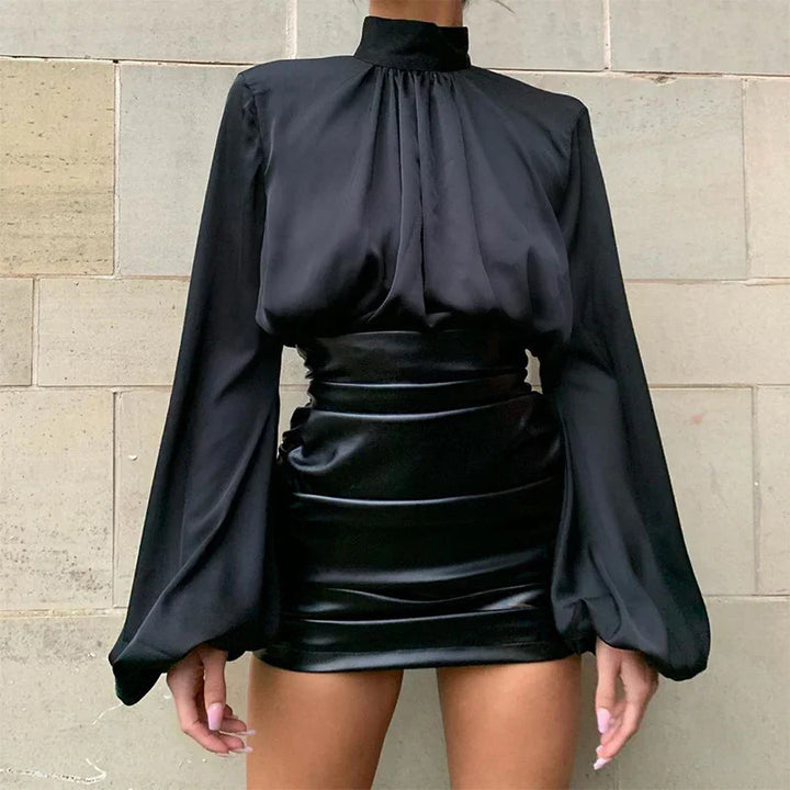 Woman wearing black high-neck long sleeve blouse with puff sleeves and black satin mini skirt