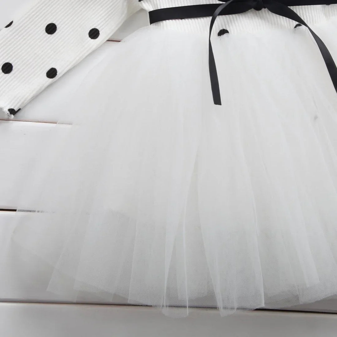 White tulle skirt with black ribbon and white top with black polka dots on white wooden background