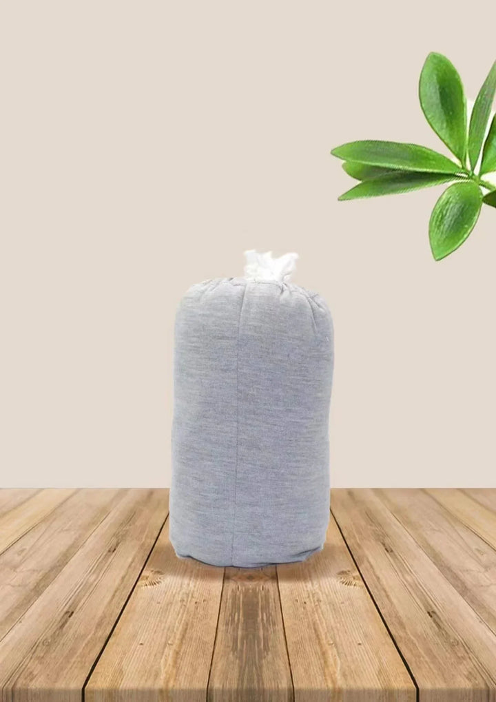 Gray fabric tissue box cover on wooden surface with green plant leaves in background