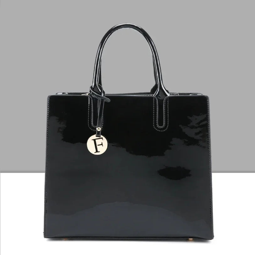 Glossy black patent leather handbag with double handles and round tag featuring letter F