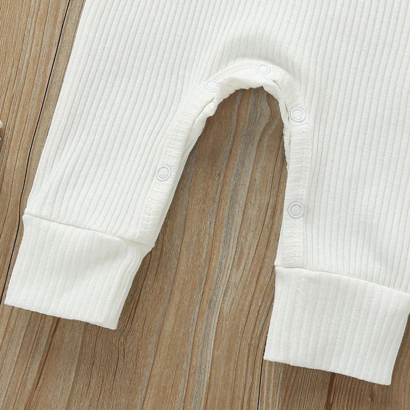 Close-up of white ribbed baby onesie with snap buttons on wood background