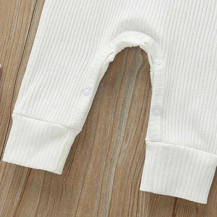 Close-up of white ribbed baby onesie with snap buttons on wood background