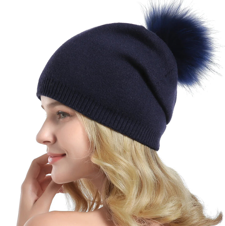 Blonde woman wearing navy blue knit beanie hat with fluffy pom pom on white background