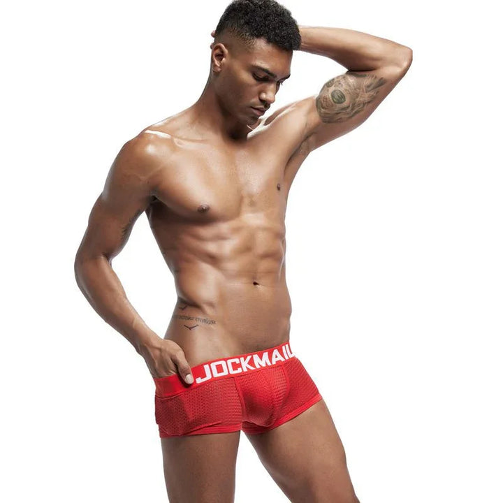 Fit male model wearing red JOCKMAIL mesh boxer briefs posing against white background