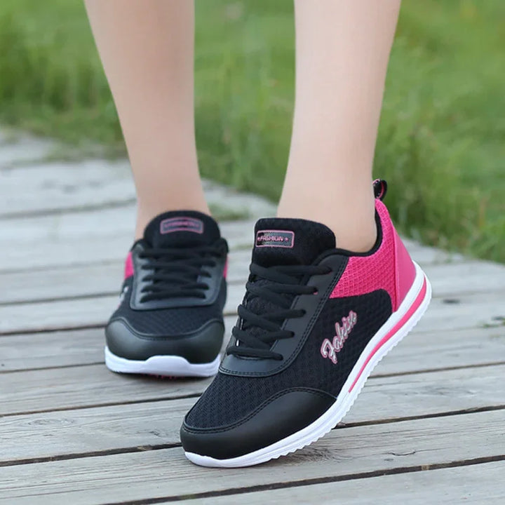 Black and pink casual sneakers with white soles worn outdoors on wooden deck