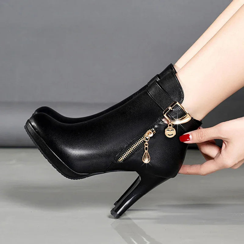 Black leather high-heeled ankle boots with gold zipper and buckle charm on model's feet