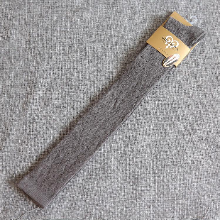 Single grey cable knit long sock with beige packaging on textured grey fabric background