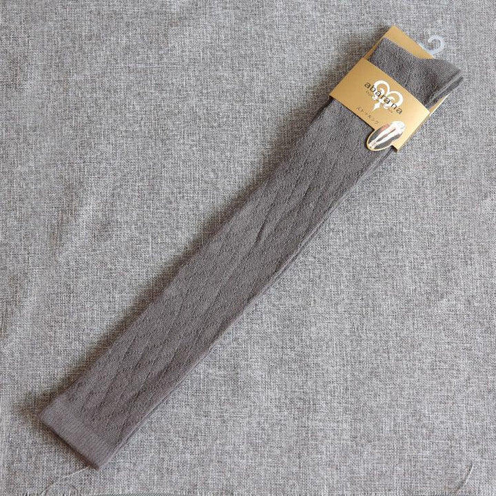 Single grey cable knit long sock with beige packaging on textured grey fabric background