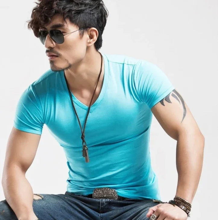 Stylish man wearing blue V-neck t-shirt, sunglasses, necklace, tattoo, and bracelets