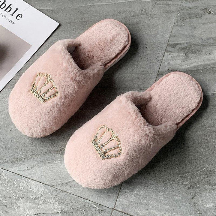 Soft pink fuzzy slippers with gold rhinestone crown decoration on gray tile floor
