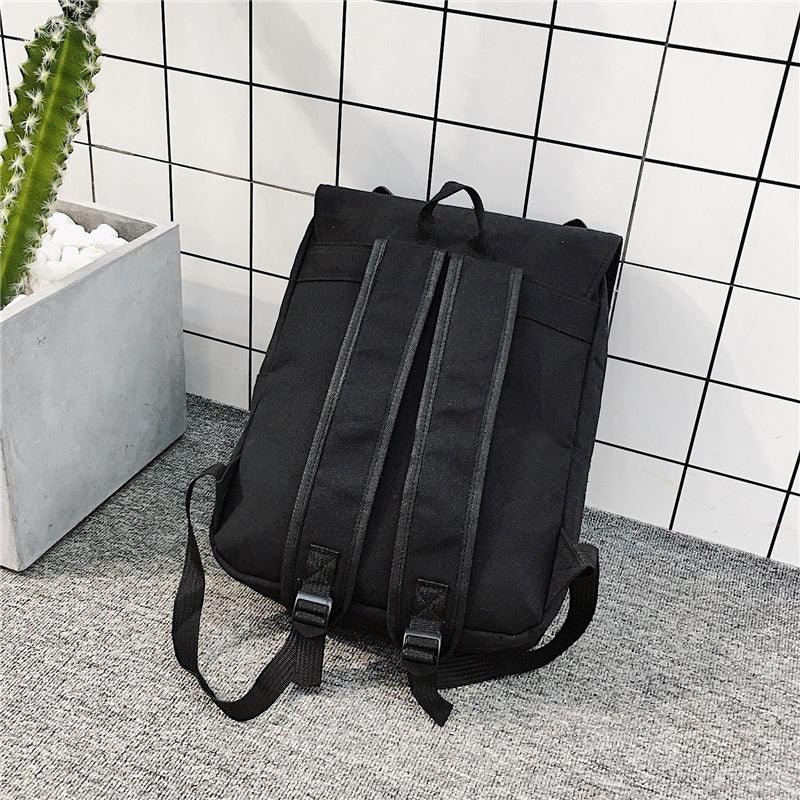 Black backpack with padded straps placed on gray carpet against white tiled wall and potted cactus