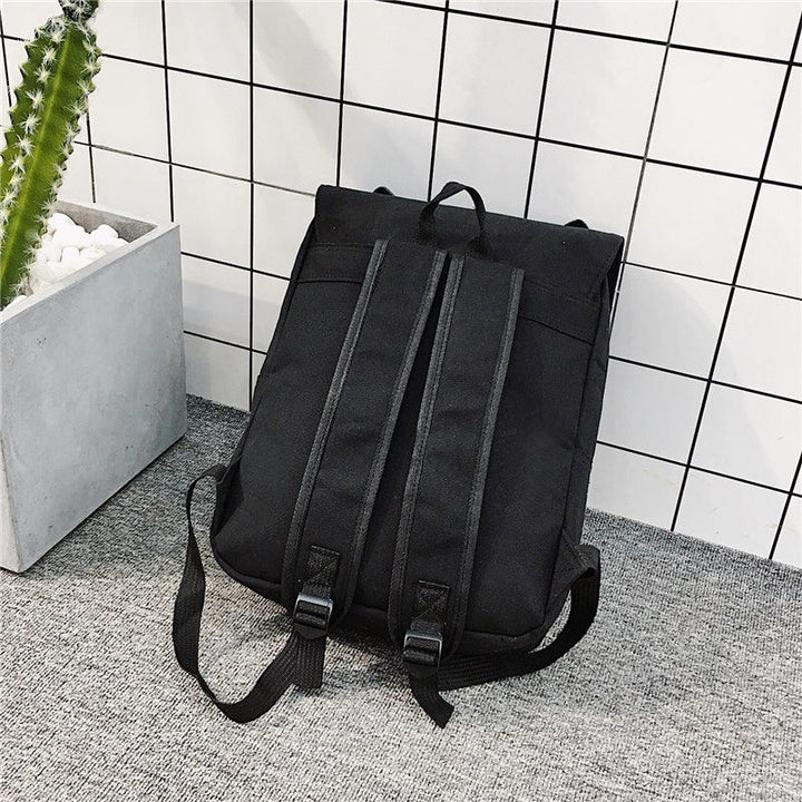 Black backpack with padded straps placed on gray carpet against white tiled wall and potted cactus