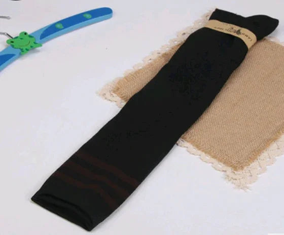 Black long socks with brown stripes folded on beige lace fabric, next to blue wooden hanger with green frog design