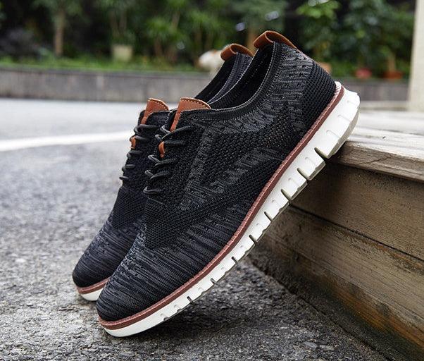 Black knitted casual shoes with white soles and brown accents displayed outdoors on pavement