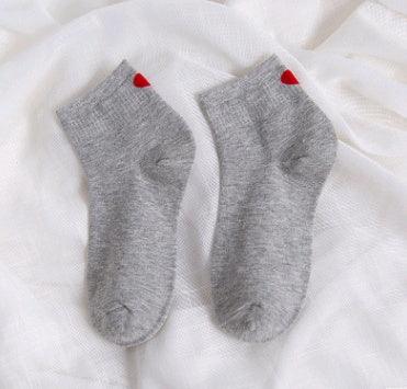 Pair of grey ankle socks with red heart detail on white fabric background