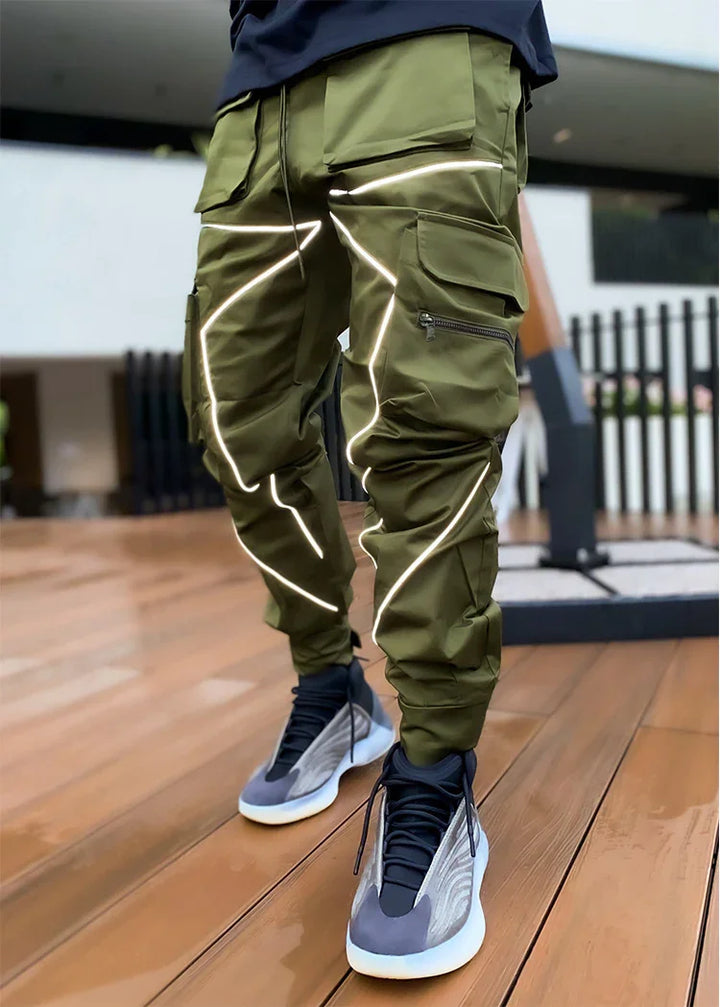 Person wearing olive green cargo pants with reflective stripes and gray high-top sneakers on wooden floor