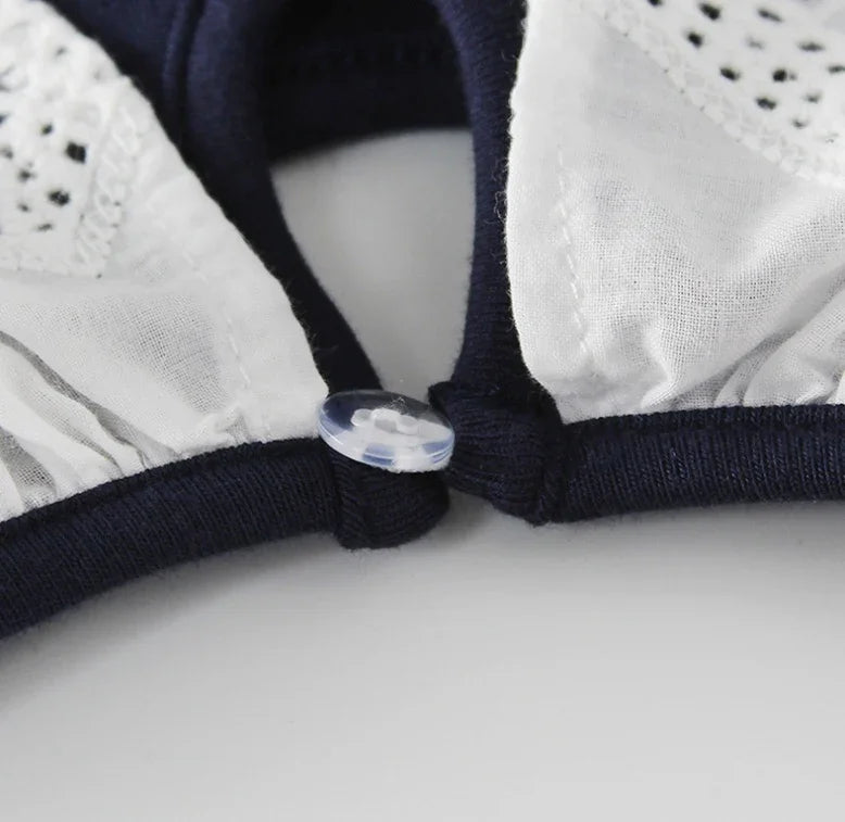 Close-up of white cotton fabric with delicate eyelet lace and dark blue trim featuring a small clear button