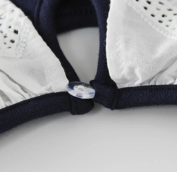 Close-up of white cotton fabric with delicate eyelet lace and dark blue trim featuring a small clear button
