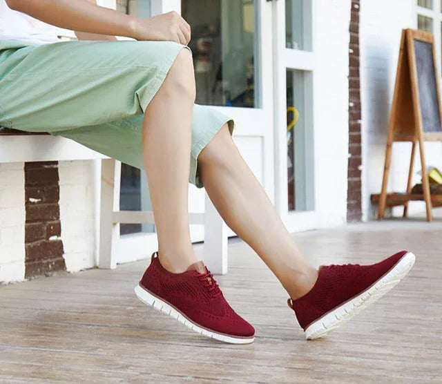 Person wearing maroon casual sneakers with white soles and light green pants sitting outdoors on wooden floor