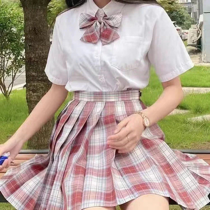 Woman wearing white short-sleeve shirt and red plaid skirt with matching bow tie sitting outdoors