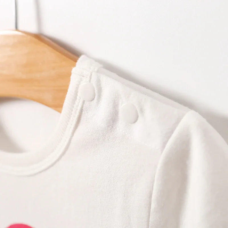 Close-up of white baby onesie with shoulder snap buttons on wooden hanger