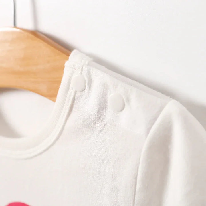 Close-up of white baby onesie with shoulder snap buttons on wooden hanger