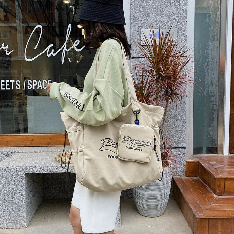 Woman in green sweater and black hat carrying beige tote bag with 'Breast Food Lover' text outside cafe