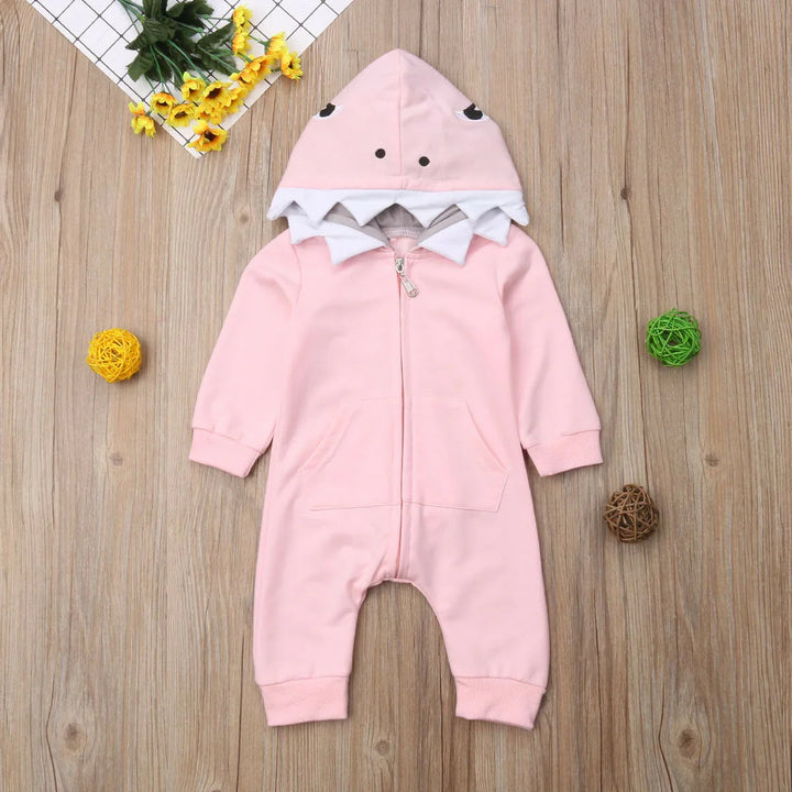 Pink baby onesie with dinosaur hood and teeth on wood background with decorative flowers and balls