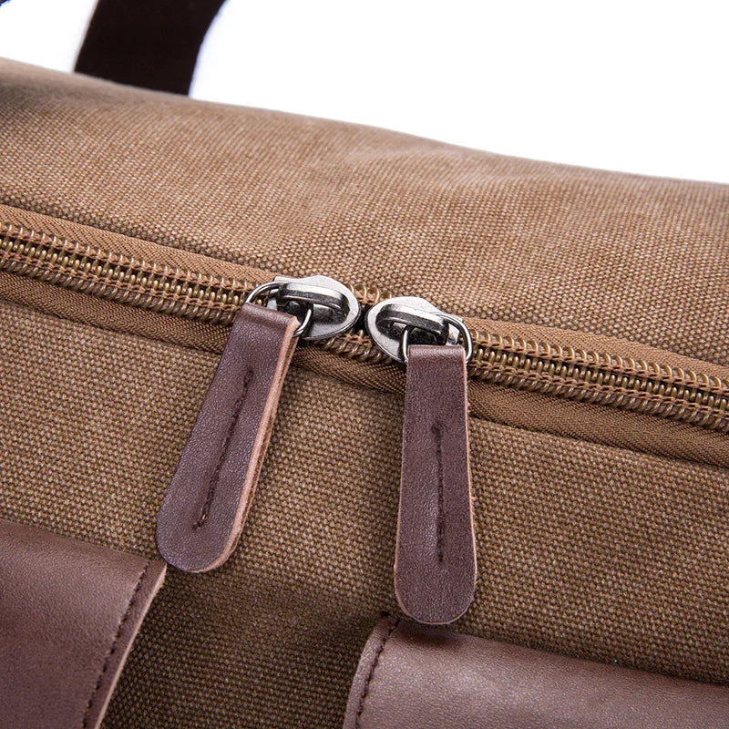 Close-up of brown canvas bag zipper with dual metal sliders and dark leather pull tabs