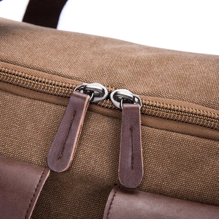 Close-up of brown canvas bag zipper with dual metal sliders and dark leather pull tabs