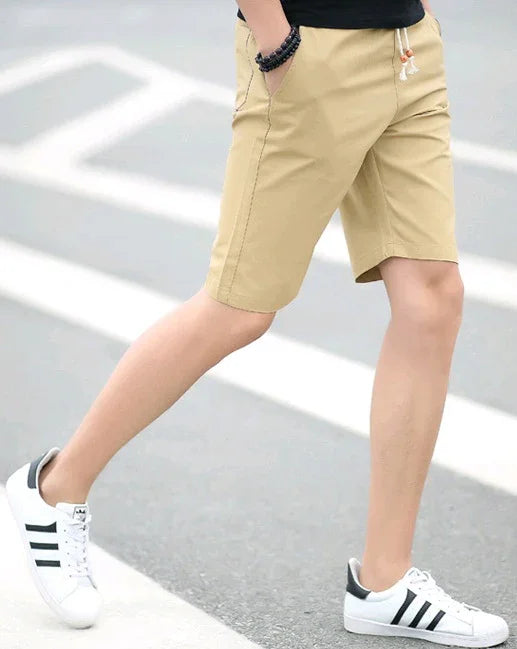 Person wearing beige casual shorts and white sneakers with black stripes walking on street