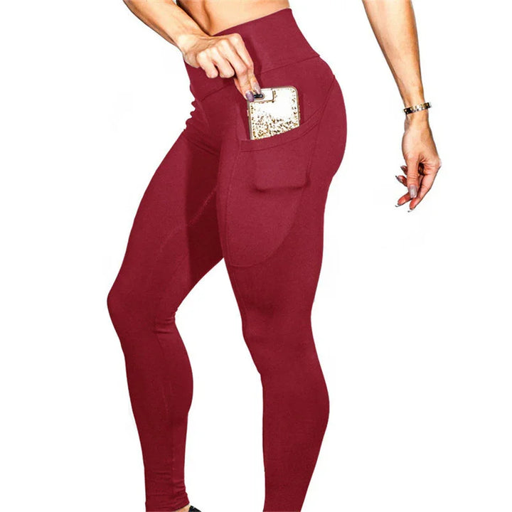Woman wearing high-waisted burgundy leggings with a side pocket holding a gold smartphone