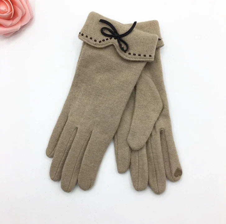 Beige wool gloves with stitched cuffs and black bow detail on white background