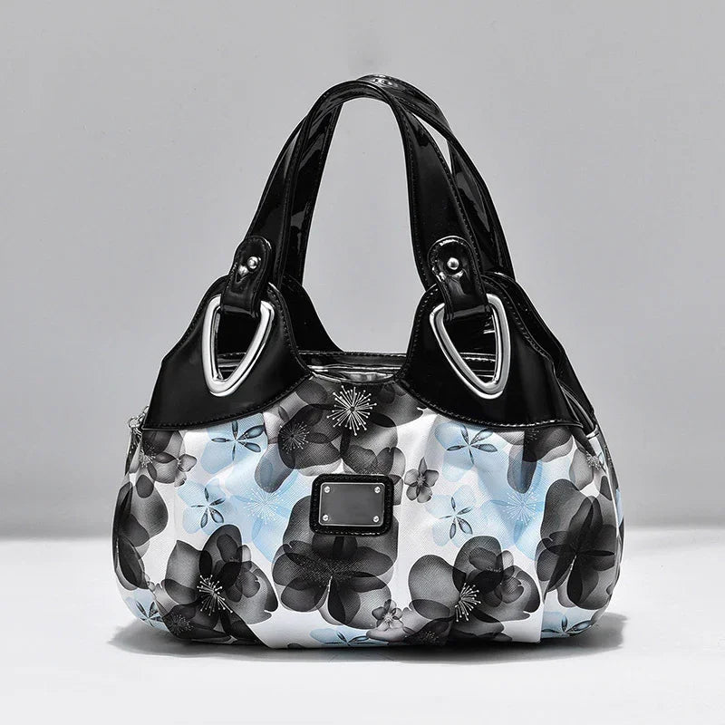 Black and white floral handbag with light blue accents and glossy black handles against gray background