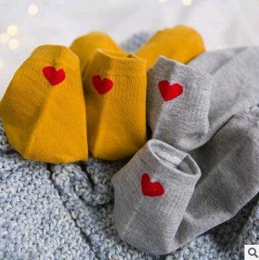 Yellow and gray baby socks with red heart embroidery on knitted gray blanket