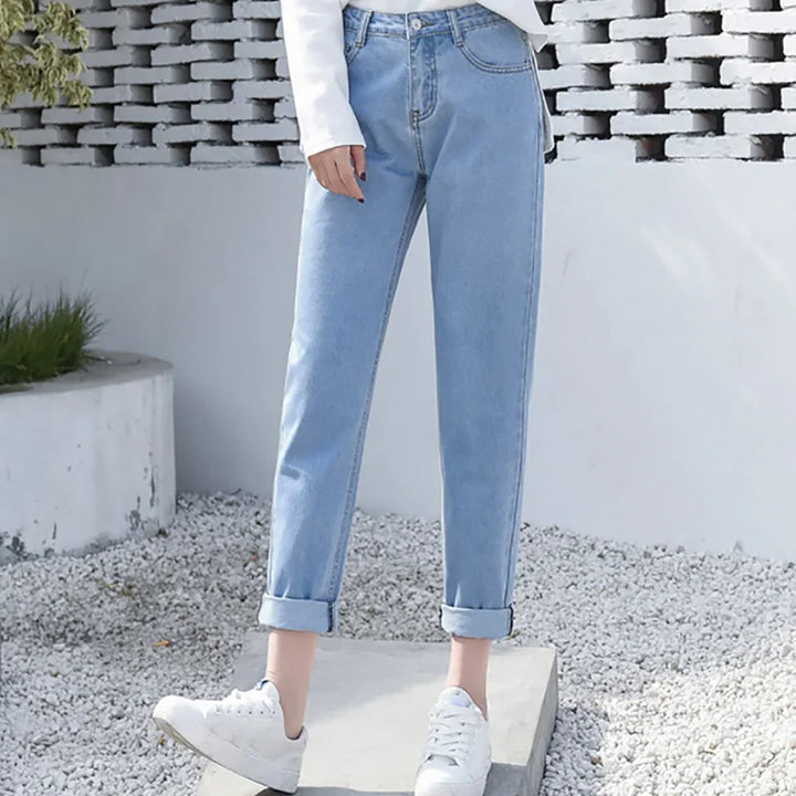 Woman wearing light blue rolled-up jeans and white sneakers standing on concrete slab outdoors