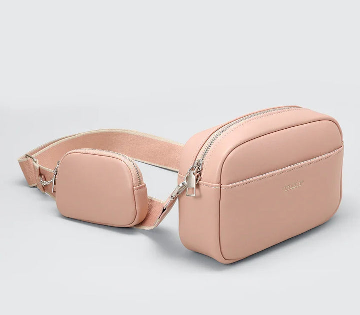 Pink leather crossbody bag with adjustable strap and small pouch on a white background