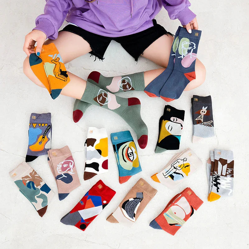 Person in purple sweatshirt and black shorts displaying colorful artistic socks with abstract and face designs