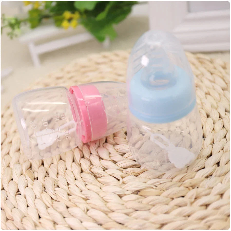 Two clear baby bottles with pink and blue caps placed on a woven mat with blurred green plant background