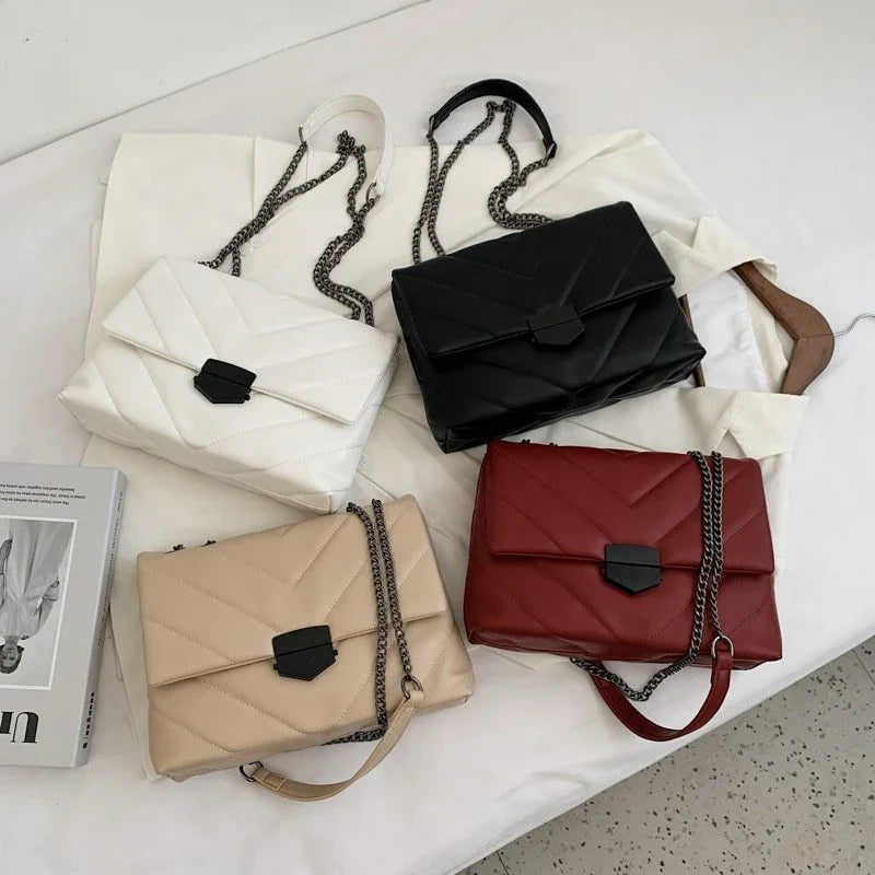 Four quilted leather handbags in white, black, beige, and red with black clasps and chain straps on a white fabric backdrop