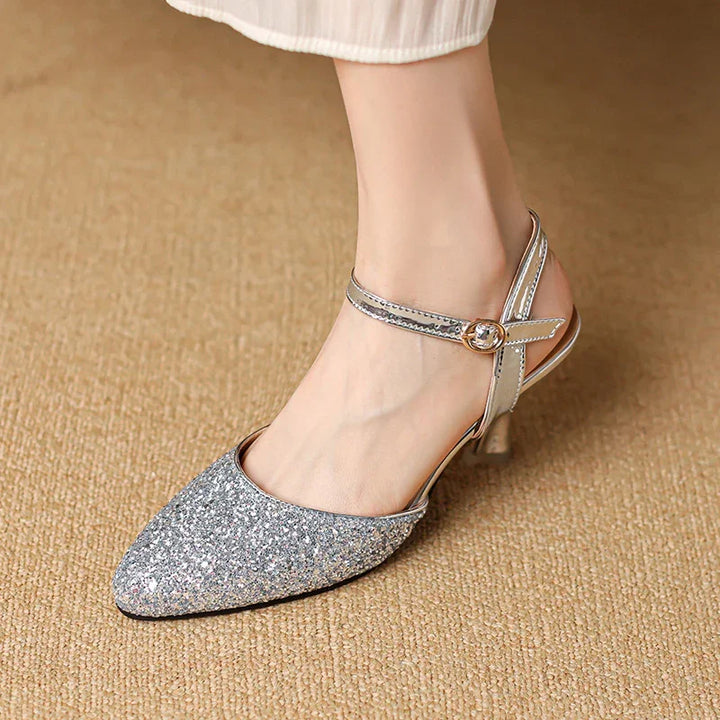 silver glitter pointed toe high heel sandal with ankle strap and gold buckle on carpet