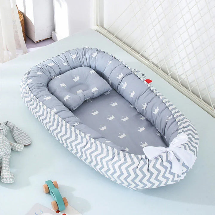 Gray baby nest with white crown pattern and chevron sides, featuring a small pillow and white bow