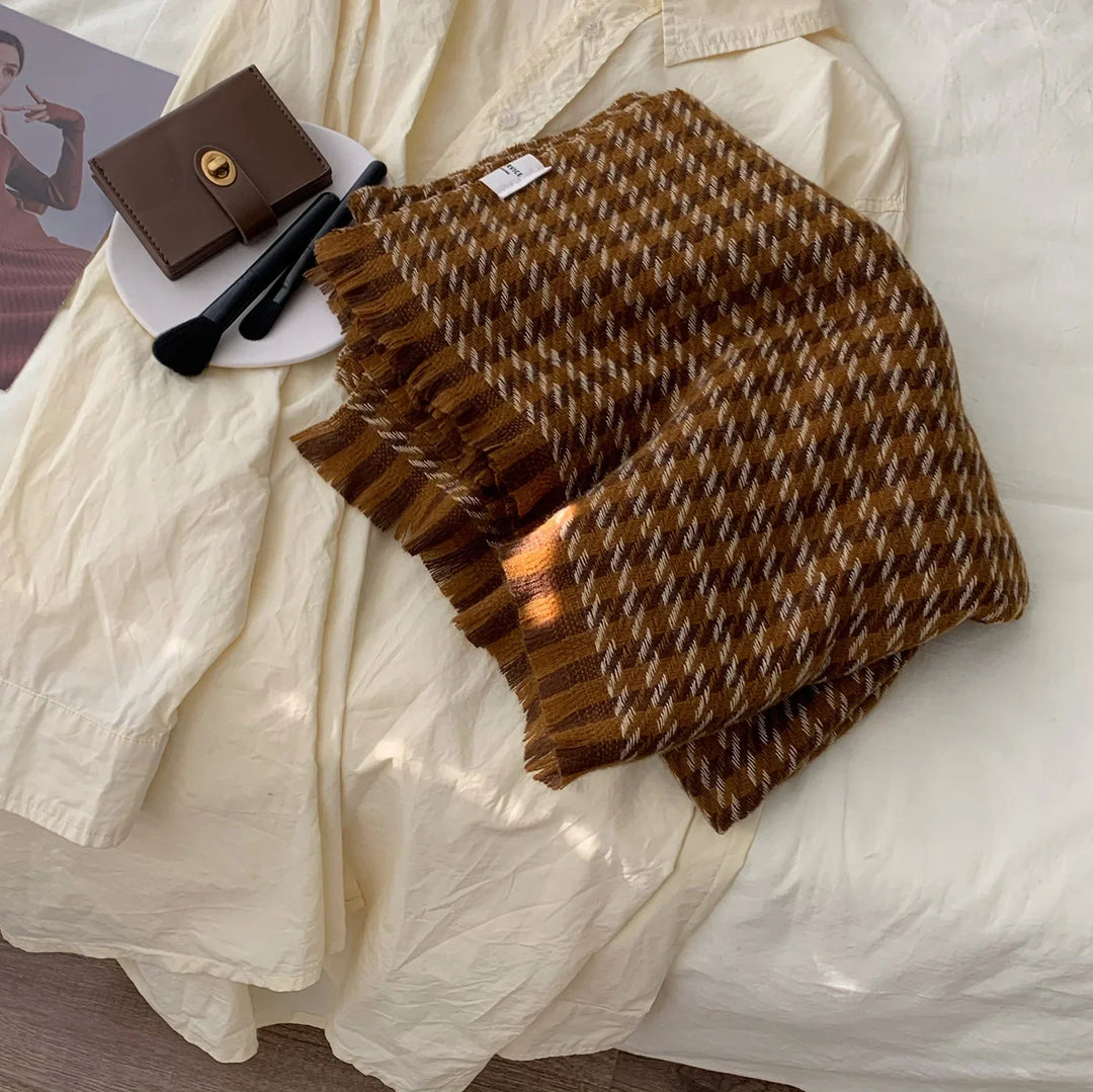 Folded brown checkered wool scarf with fringe on cream fabric next to brown wallet and makeup brushes on white plate
