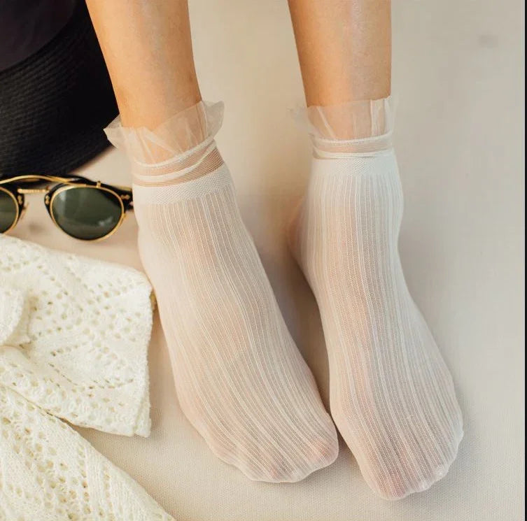 Close-up of feet wearing sheer white textured ankle socks with ruffled edges, next to sunglasses and lace fabric