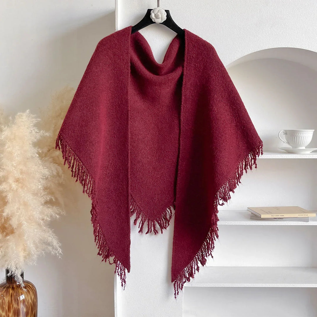 Burgundy wool poncho with fringe edges hanging on black hanger in minimalist interior