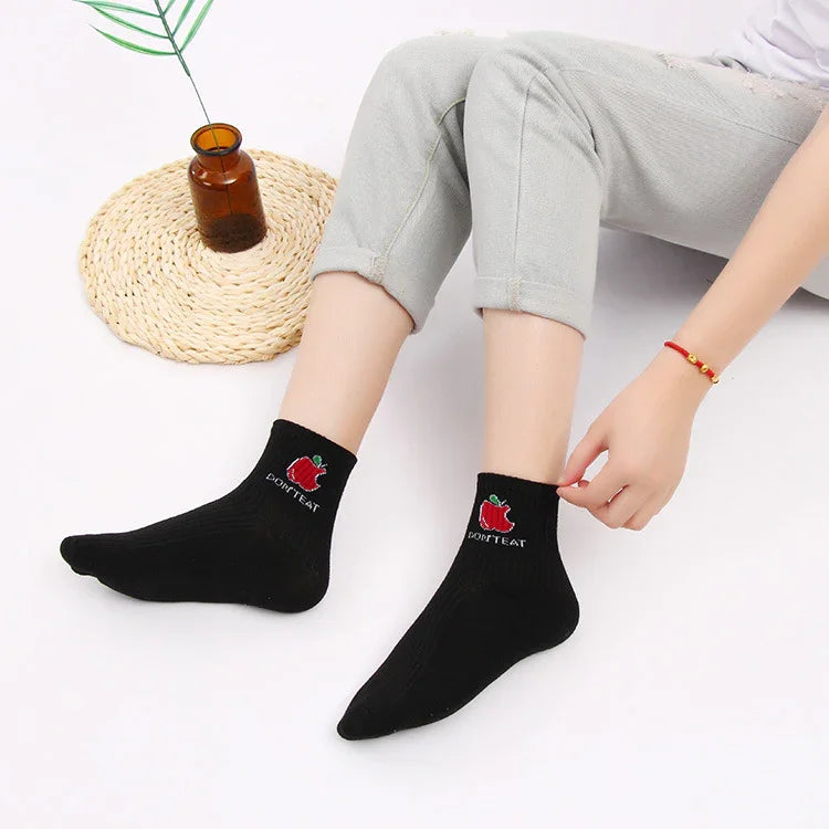 Person wearing black ankle socks with red apple and text 'DON'T EAT' sitting on white floor with brown vase on woven mat